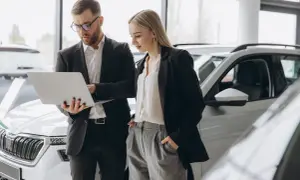 Uomo e donna in un concessionario auto esaminano le specifiche di una nuova macchina aziendale su un laptop.