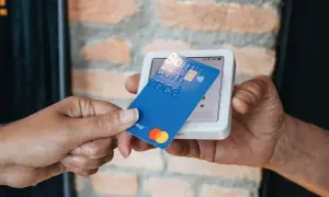 Pagamento contactless con carta blu su POS. La carta mostra "Soma com você" e i loghi Mastercard e Visa.
