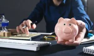Uomo con salvadanaio rosa calcola come investire i risparmi oggi, con tastiera e calcolatrice a portata di mano.