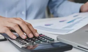 Mani che usano una calcolatrice e fogli con grafici, per gestire le spese, come quelle delle carte carburante ricaricabili.