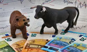 A bull and bear figurine face each other on euro banknotes and stock charts.