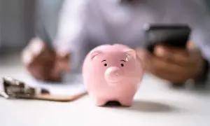 Un salvadanaio BPER rosa, simbolo di risparmio, su una scrivania mentre una persona scrive e usa il telefono.