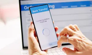 Mani che effettuano un bonifico istantaneo BPER tramite smartphone, con schermo che mostra "Transferring 20.00 to Friend Joe".