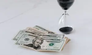 Soldi e clessidra su sfondo bianco, un promemoria che il tempo è denaro e che ogni momento conta per il nostro orizzonte temporale.