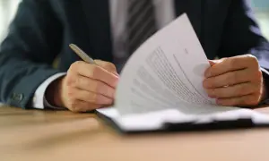 Uomo in giacca e cravatta firma un documento, parte di un set informativo.