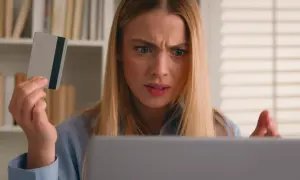 Ragazza confusa guarda il laptop, tenendo una carta di credito, preoccupata per un addebito sul conto.