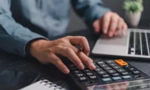 Mani che digitano su calcolatrice e tastiera, pianificando la partita IVA forfettaria.