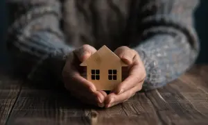 Mani che proteggono una casetta di legno, simbolo di sicurezza e del valore di una polizza CPI.