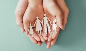 Mani che proteggono una famiglia di carta, simbolo di sicurezza e assicurazione premorienza per i propri cari.