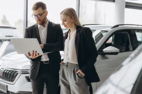 Uomo e donna in un concessionario auto esaminano le specifiche di una nuova macchina aziendale su un laptop.