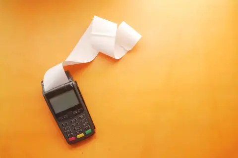 POS con scontrino lungo su sfondo arancione. Utile per una tabella costi deducibili professionisti.