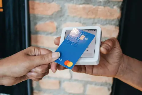 Pagamento contactless con carta blu su POS. La carta mostra "Soma com você" e i loghi Mastercard e Visa.