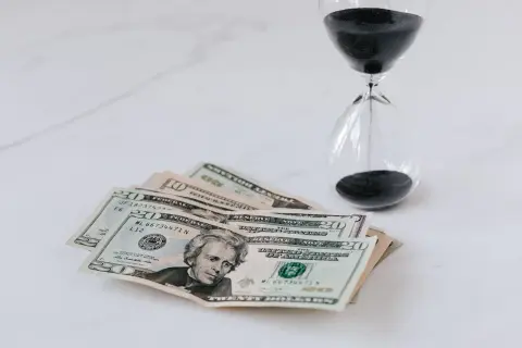 Soldi e clessidra su sfondo bianco, un promemoria che il tempo è denaro e che ogni momento conta per il nostro orizzonte temporale.