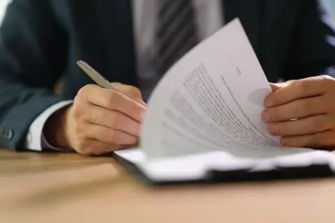 Uomo in giacca e cravatta firma un documento, parte di un set informativo.