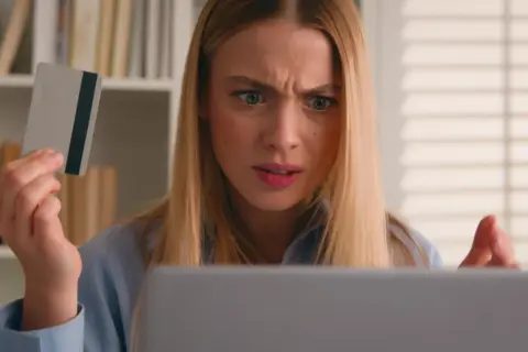 Ragazza confusa guarda il laptop, tenendo una carta di credito, preoccupata per un addebito sul conto.
