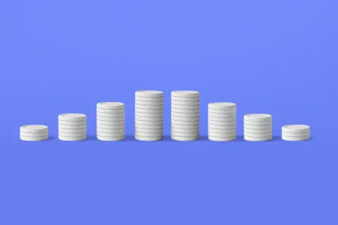 Pile di monete bianche su sfondo blu, che illustrano il deflazione significato con un calo dei valori.