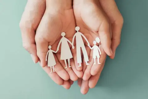 Mani che proteggono una famiglia di carta, simbolo di sicurezza e assicurazione premorienza per i propri cari.