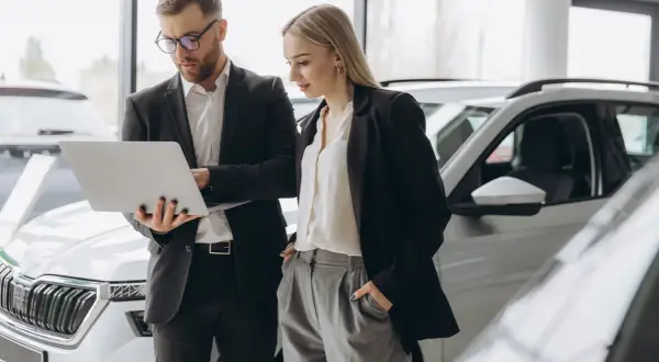 Uomo e donna in un concessionario auto esaminano le specifiche di una nuova macchina aziendale su un laptop.