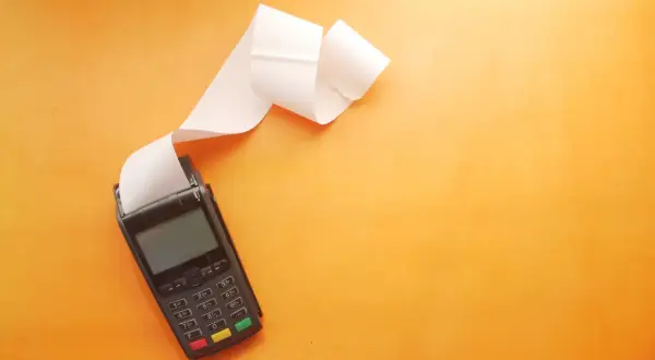POS con scontrino lungo su sfondo arancione. Utile per una tabella costi deducibili professionisti.