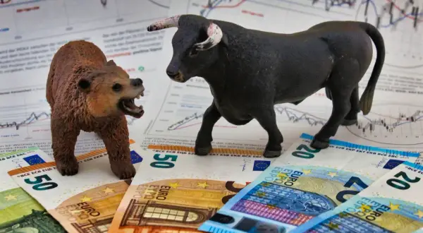A bull and bear figurine face each other on euro banknotes and stock charts.