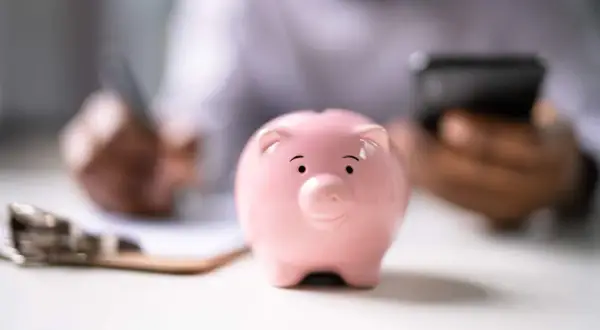 Un salvadanaio BPER rosa, simbolo di risparmio, su una scrivania mentre una persona scrive e usa il telefono.