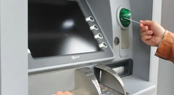 Mano inserisce una carta in un bancomat per versare contanti in banca.