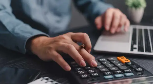 Mani che digitano su calcolatrice e tastiera, pianificando la partita IVA forfettaria.