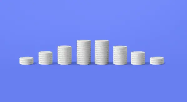 Pile di monete bianche su sfondo blu, che illustrano il deflazione significato con un calo dei valori.
