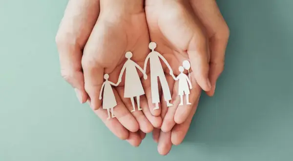 Mani che proteggono una famiglia di carta, simbolo di sicurezza e assicurazione premorienza per i propri cari.