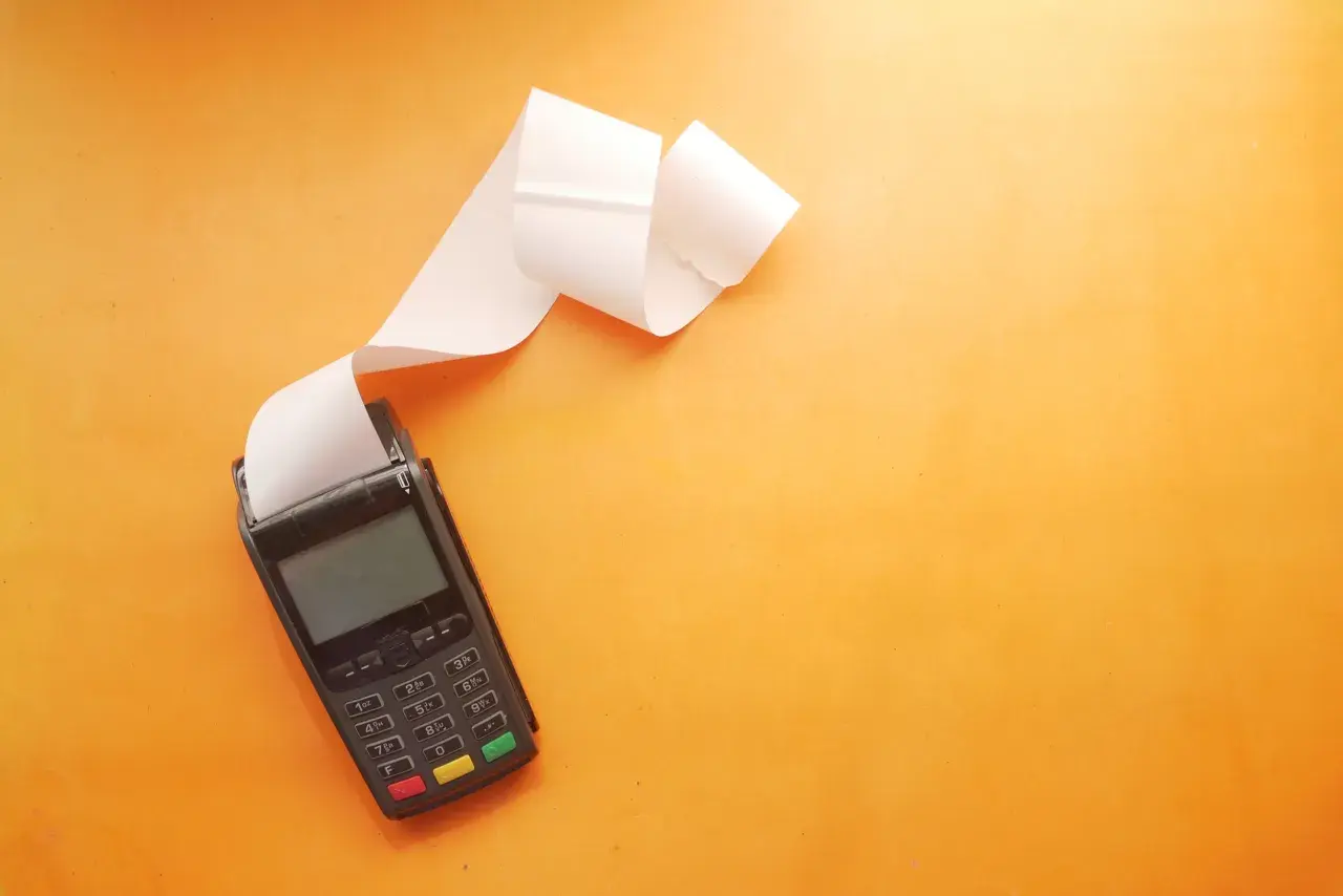 POS con scontrino lungo su sfondo arancione. Utile per una tabella costi deducibili professionisti.