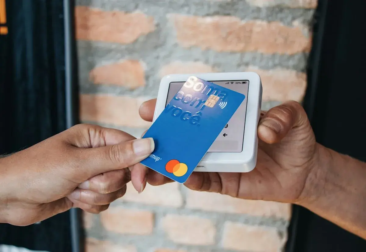 Pagamento contactless con carta blu su POS. La carta mostra "Soma com você" e i loghi Mastercard e Visa.