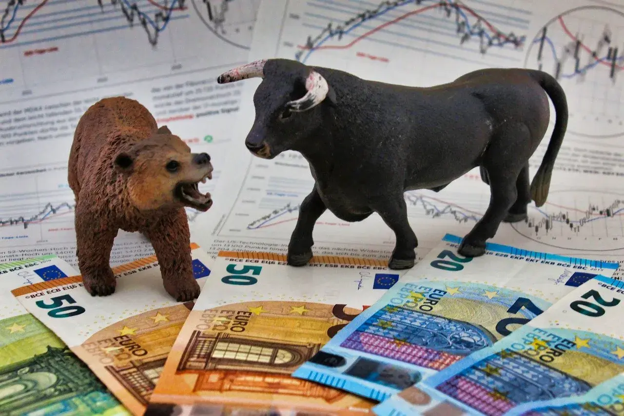 A bull and bear figurine face each other on euro banknotes and stock charts.