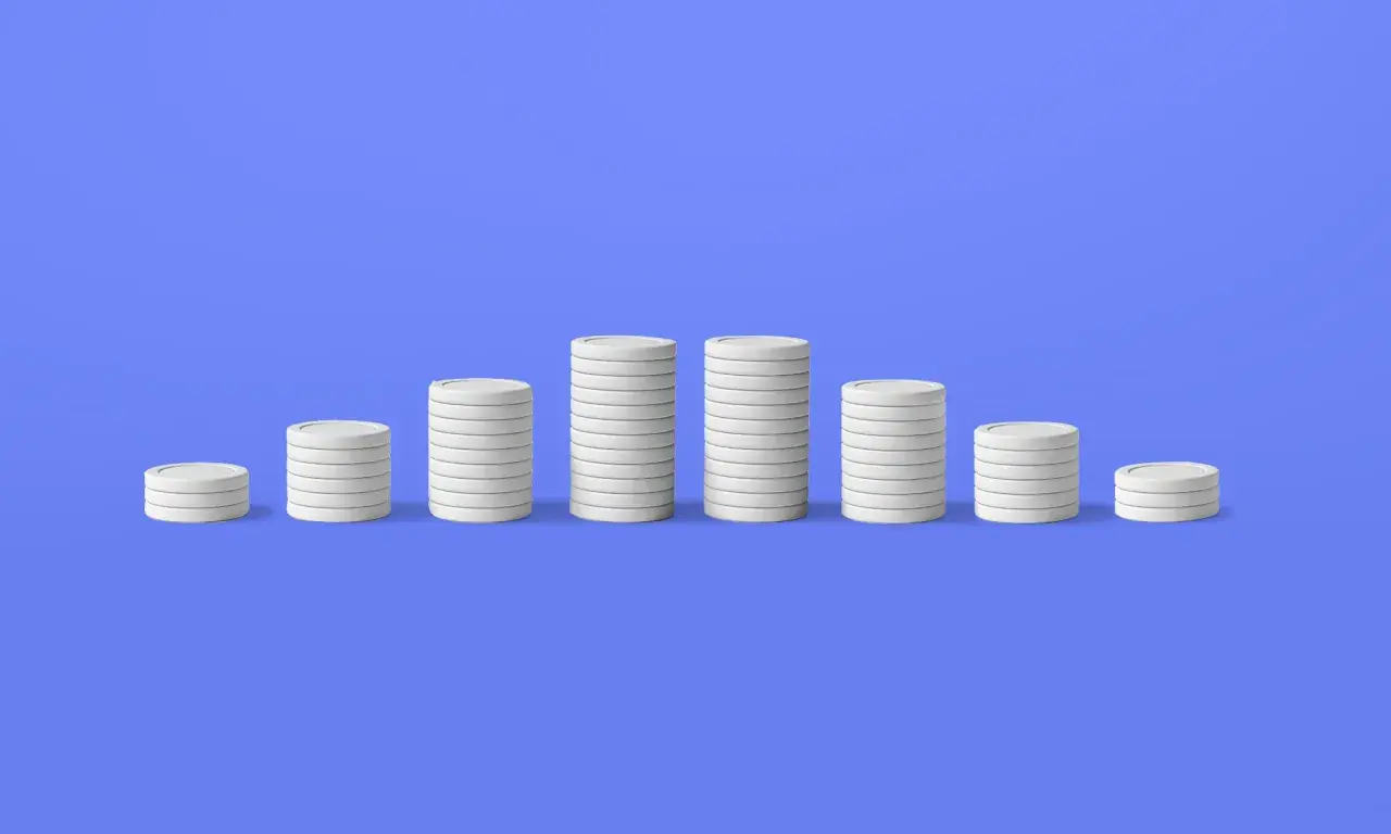 Pile di monete bianche su sfondo blu, che illustrano il deflazione significato con un calo dei valori.