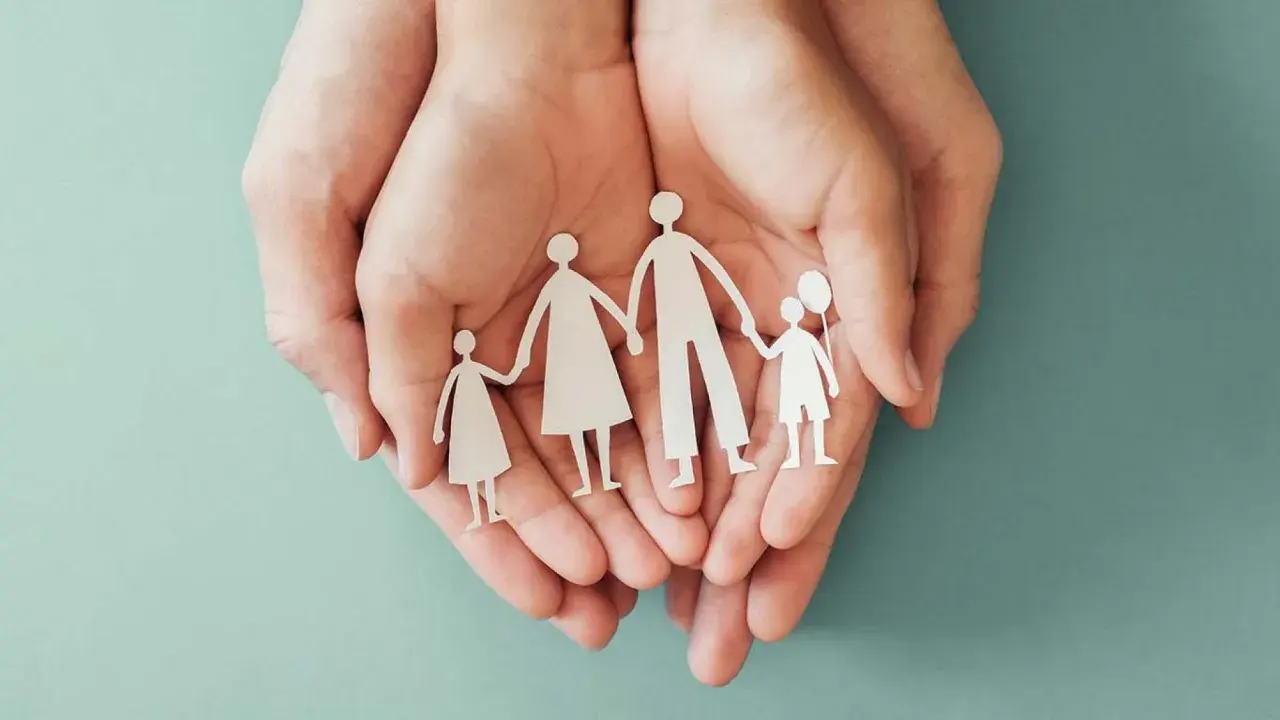 Mani che proteggono una famiglia di carta, simbolo di sicurezza e assicurazione premorienza per i propri cari.