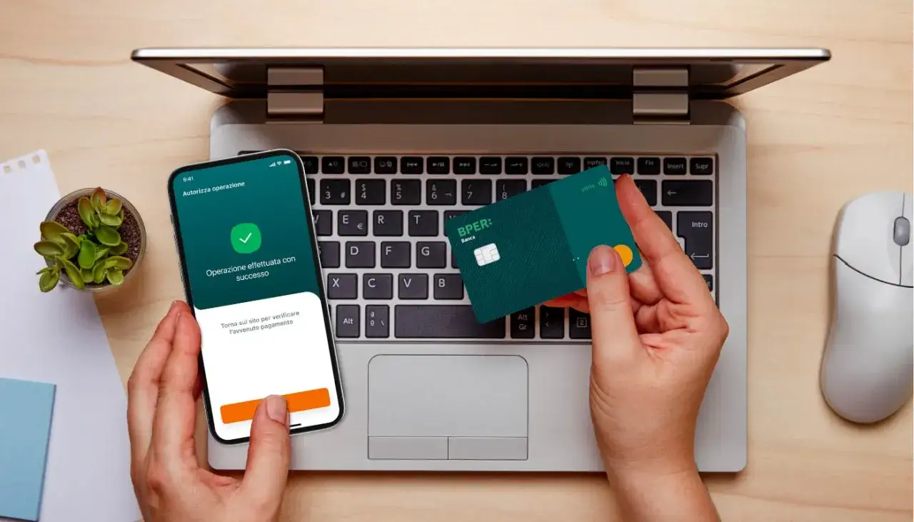 Pagamento online autorizzato con successo tramite app BPER Banca. Una carta verde BPER è tenuta sopra la tastiera di un laptop.
