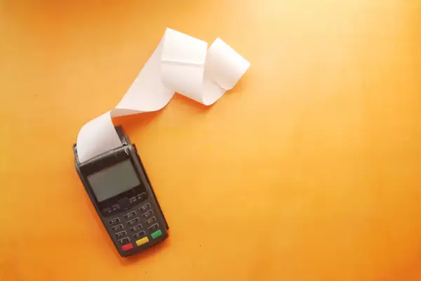 POS con scontrino lungo su sfondo arancione. Utile per una tabella costi deducibili professionisti.