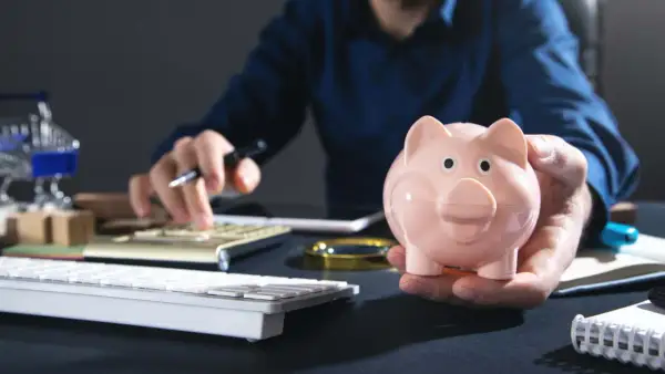 Uomo con salvadanaio rosa calcola come investire i risparmi oggi, con tastiera e calcolatrice a portata di mano.