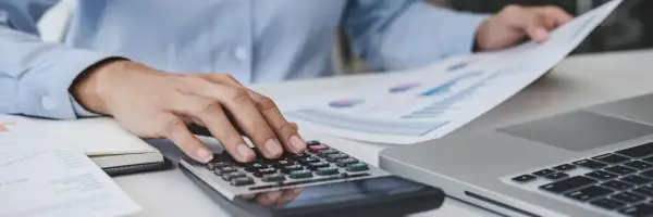 Mani che usano una calcolatrice e fogli con grafici, per gestire le spese, come quelle delle carte carburante ricaricabili.
