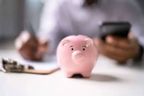 Un salvadanaio BPER rosa, simbolo di risparmio, su una scrivania mentre una persona scrive e usa il telefono.