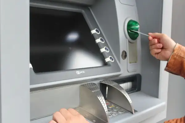Mano inserisce una carta in un bancomat per versare contanti in banca.