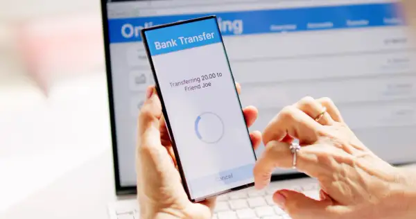 Mani che effettuano un bonifico istantaneo BPER tramite smartphone, con schermo che mostra "Transferring 20.00 to Friend Joe".