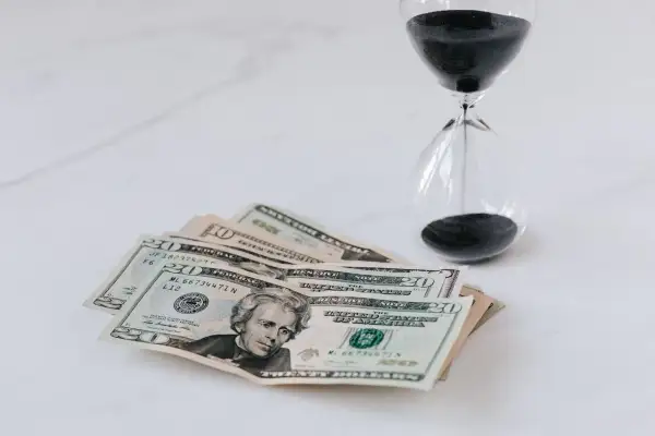 Soldi e clessidra su sfondo bianco, un promemoria che il tempo è denaro e che ogni momento conta per il nostro orizzonte temporale.