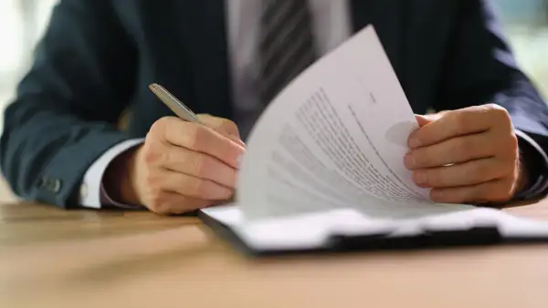 Uomo in giacca e cravatta firma un documento, parte di un set informativo.