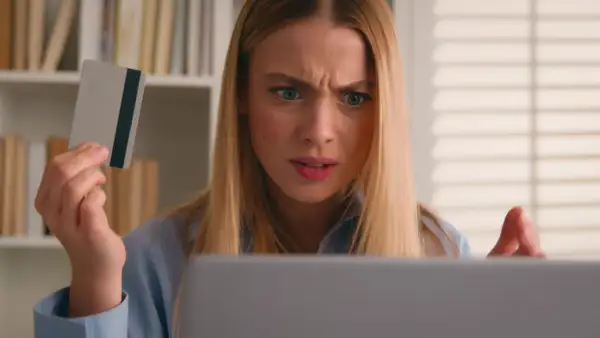 Ragazza confusa guarda il laptop, tenendo una carta di credito, preoccupata per un addebito sul conto.