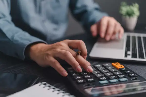 Mani che digitano su calcolatrice e tastiera, pianificando la partita IVA forfettaria.