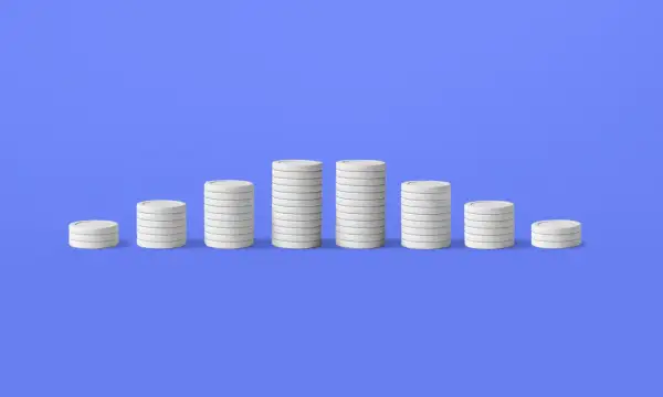 Pile di monete bianche su sfondo blu, che illustrano il deflazione significato con un calo dei valori.